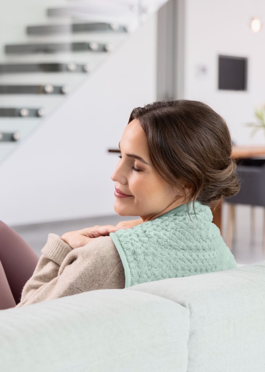 Woman relaxing with a green-colored medisana heated pad draped over her shoulders.